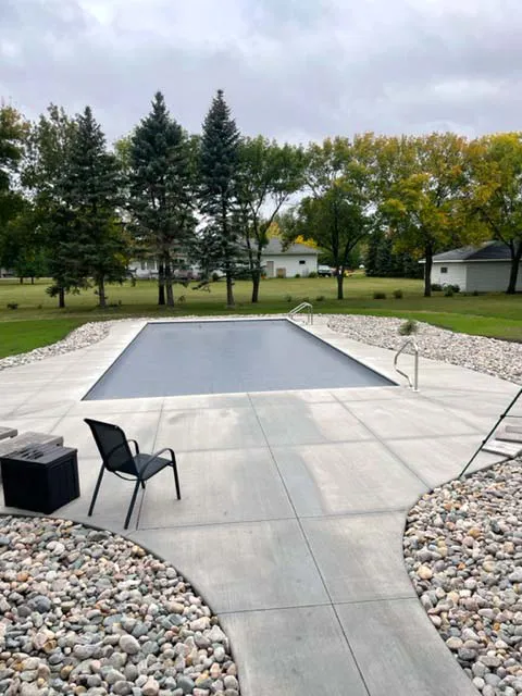 A nicely designed concrete pool deck with landscape rock and trees